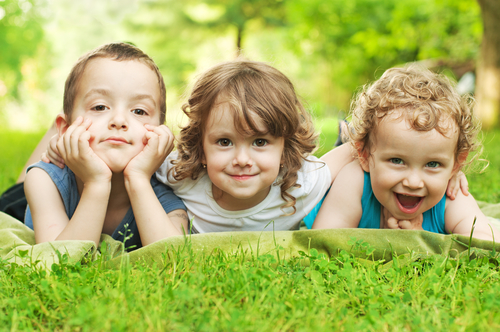 Three happy children resting on the green grass