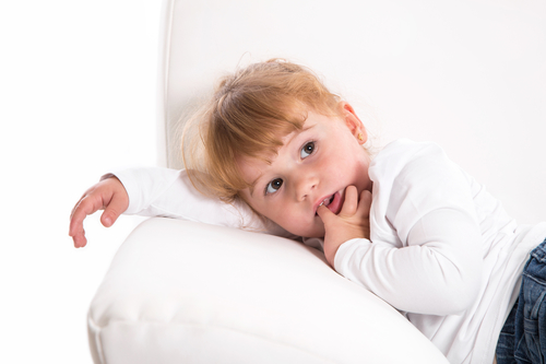 Cute child - shy girl lying on white sofa sucking thumb or finger - strawberry blonde